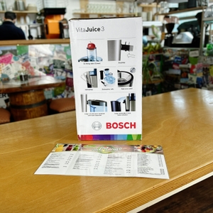 Die Seitenansicht der Verpackung des Bosch VitaJuice 3 MES3500 zeigt technische Details wie die XL-Einfüllöffnung, den Tropfstopp und den großen Tresterbehälter. Das Gerät ist als schematische Abbildung mit erklärenden Icons dargestellt.