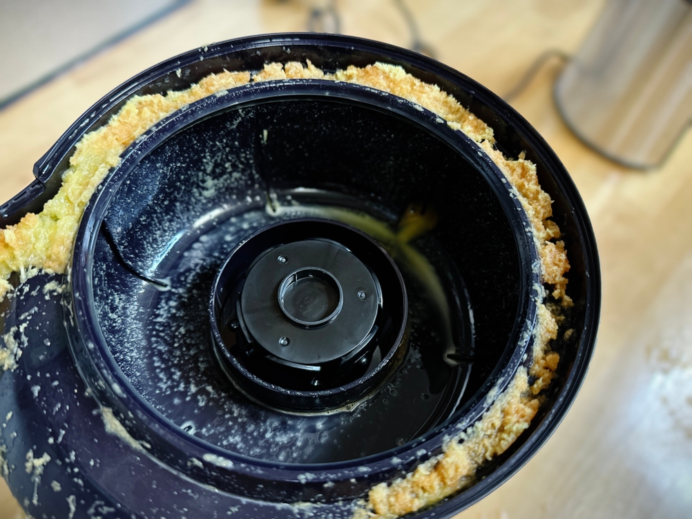 Der Tresterbehälter des Bosch VitaJuice 3 MES3500 nach der Nutzung mit Fruchtfleischresten und Saftspritzern. Der schwarze Kunststoffbehälter ist an den Rändern mit Tresterablagerungen versehen.
