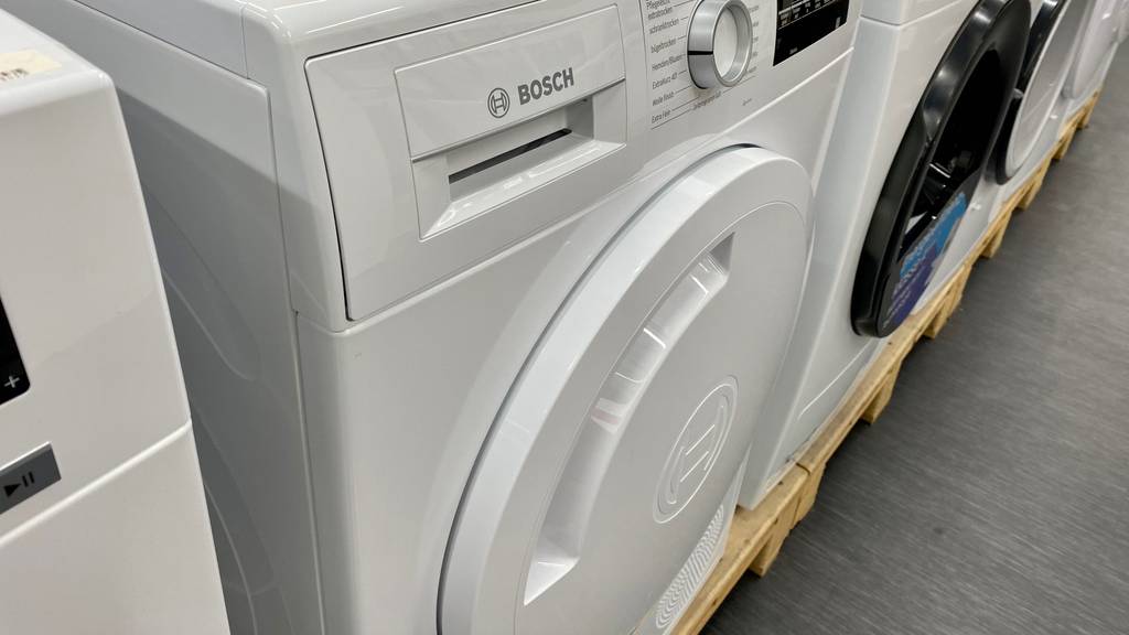 Ein getesteter Wärmepumpentrockner mit 8 kg Ladekapazität steht neben weiteren Trocknern in einem Ausstellungsbereich.