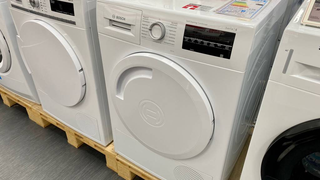 Wärmepumpentrockner-8-kg im Test: ein weißes Modell von Bosch mit Anzeige und Wahlregler steht inmitten anderer Waschmaschinen im Verkaufsbereich.