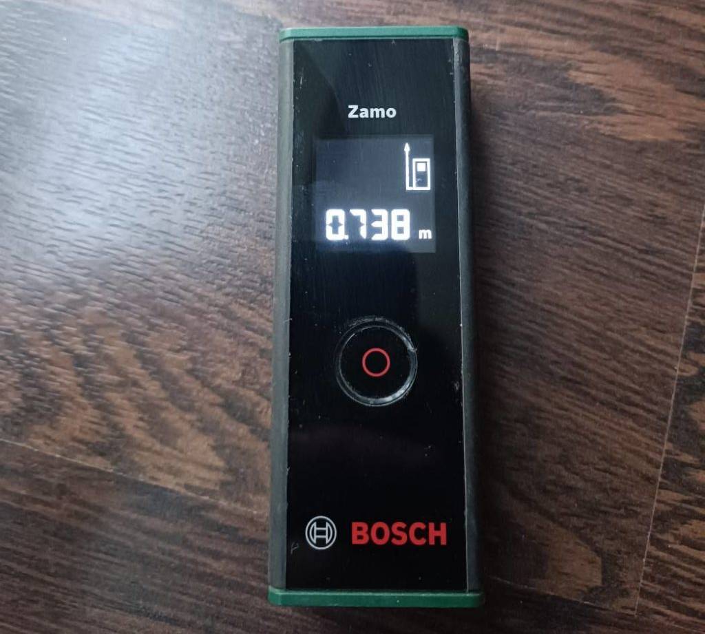 Laser-Entfernungsmesser-Test: eingeschaltetes Modell Zamo der Marke Bosch inklusive Display auf dunklem Untergrund.