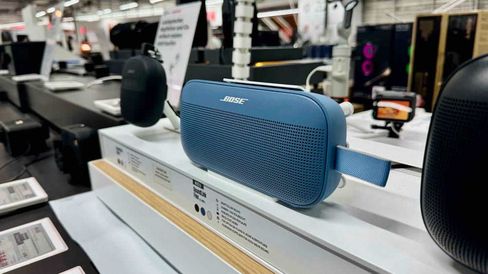 Der getestete Bose-Lautsprecher zwischen anderen Geräten auf einem Verkaufsregal.