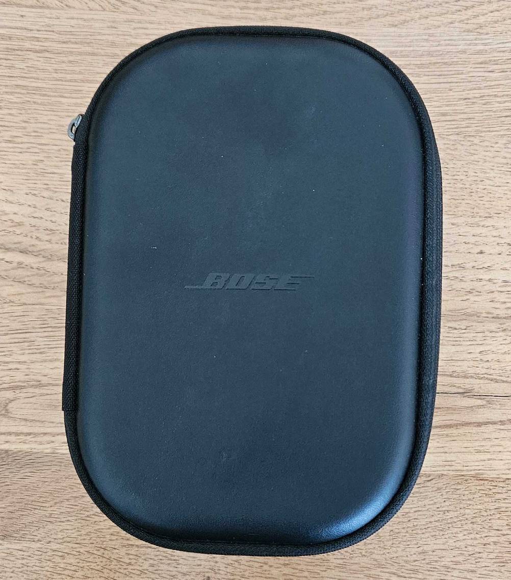 Eine schwarze Aufbewahrungstasche für getestete Over-Ear-Kopfhörer liegt geschlossen auf einer Holzfläche.