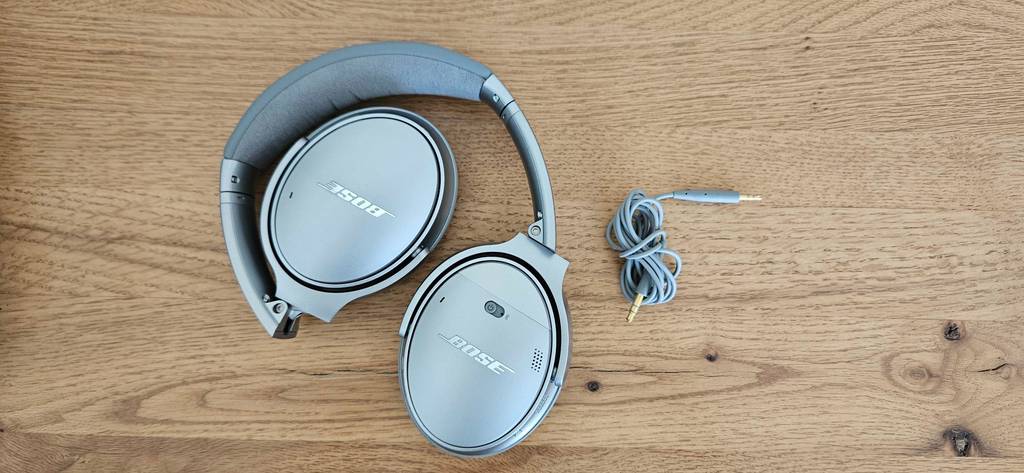Ein silberfarbener Over-Ear-Kopfhörer liegt im Test neben seinem Anschlusskabel auf einer Holzoberfläche.