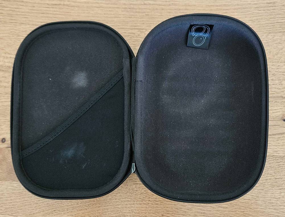Eine geöffnete, schwarze Aufbewahrungstasche für Over-Ear-Kopfhörer liegt auf einer Holzoberfläche im Test.