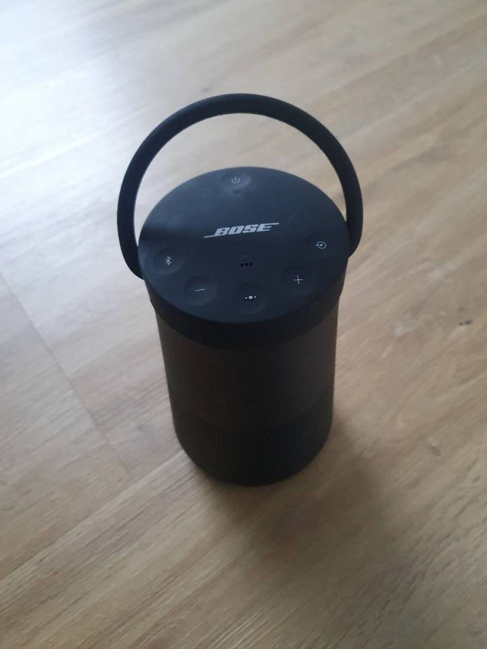 Ein schwarzer Bose-Lautsprecher steht auf einem Holzboden mit Griff sichtbar nach oben zeigend.