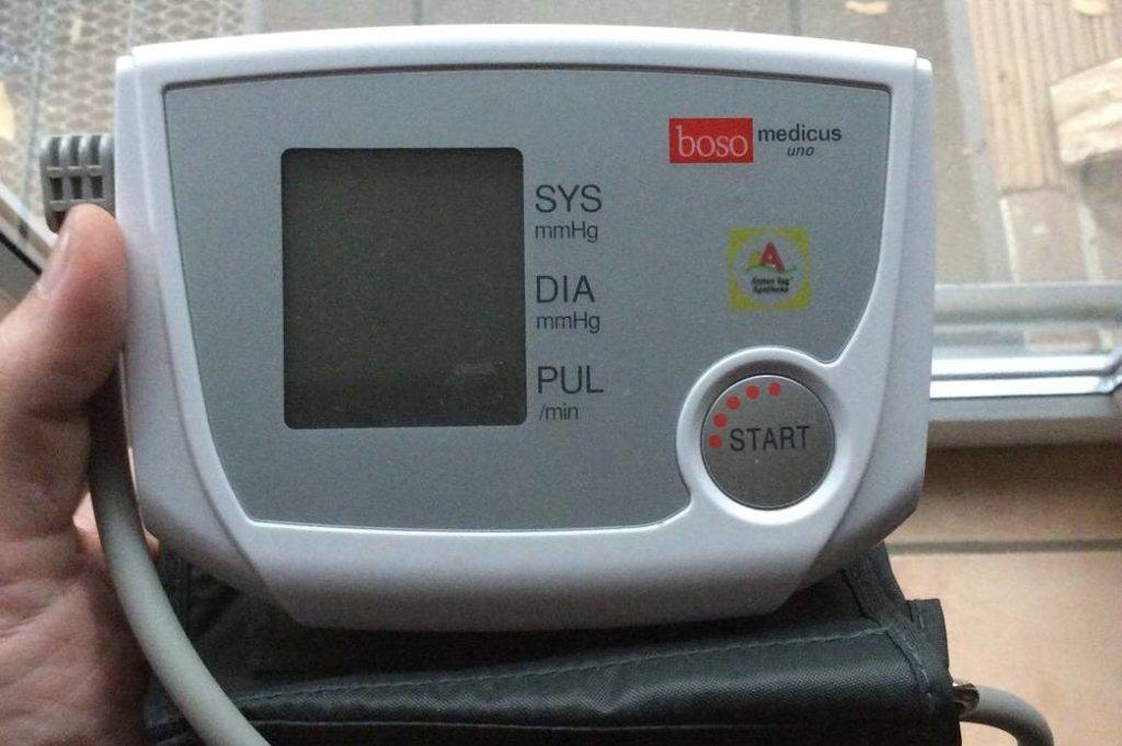 Boso Medicus Uno Blutdruckmessgerät im Test: Vorderansicht eines hellen Modells inklusive Manschette in einer linken Hand.
