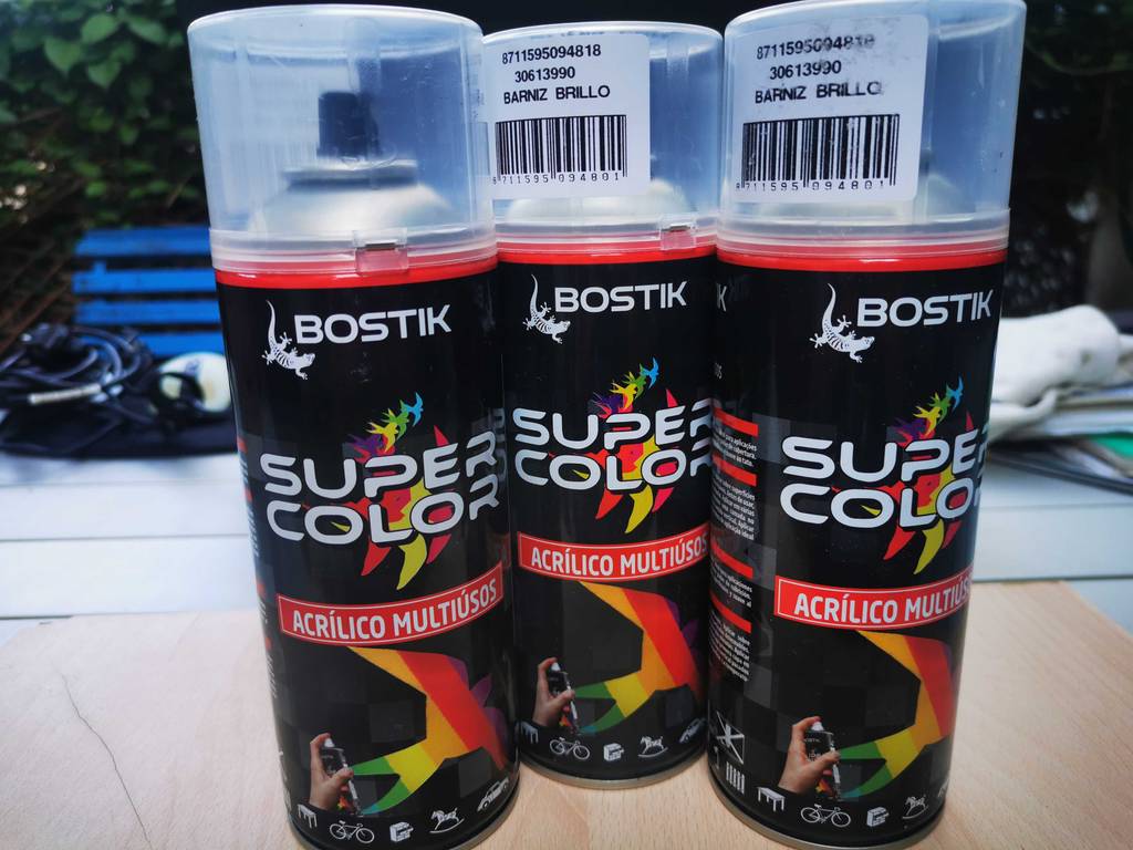 Drei Spraydosen mit Autolack-Sprays im Test stehen nebeneinander auf einer Holzplatte.