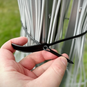 Eine Hand hält einen Kabelbinder, der um die Wäschespinne gespannt ist, fest.