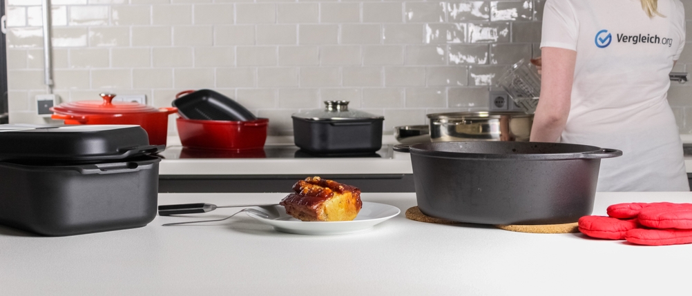 Verschiedene Bräter im Test samt fertigem Stück Fleisch auf einem Teller.