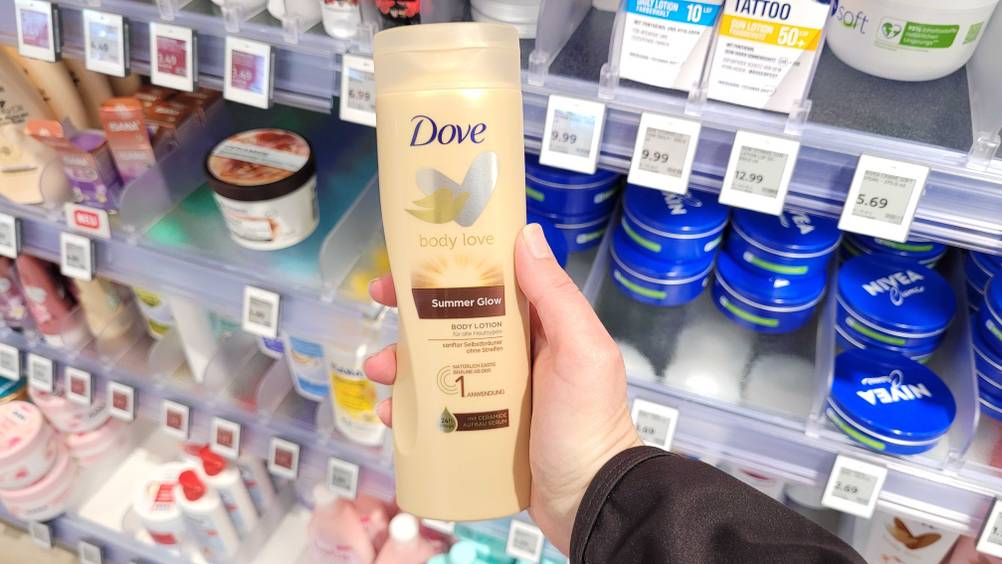 Bräunende Bodylotion im Test: Eine Hand hält eine Flasche vor ein Regal.