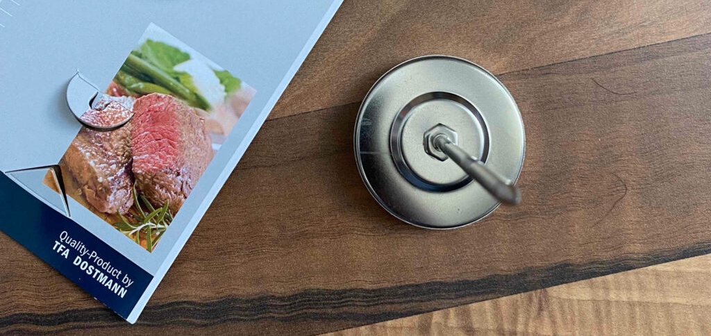 Bratenthermometer-Test: Thermometer und Verpackung liegen auf Holzuntergrund.