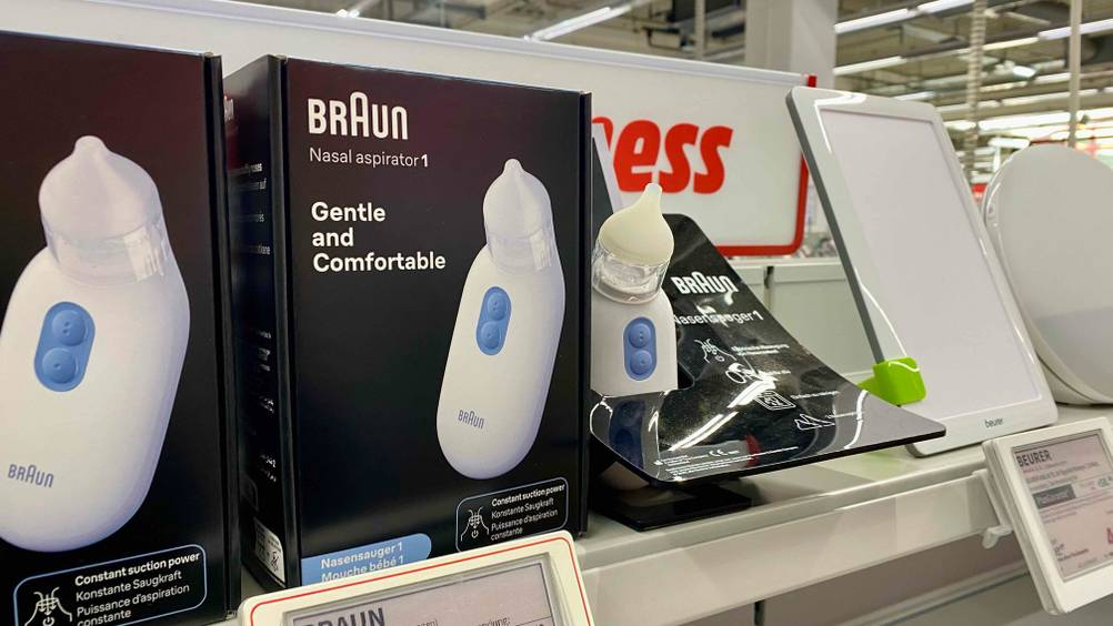 Ein getesteter elektrischer Nasensauger in einem Ständer auf einem Verkaufsregal neben der Originalverpackung.