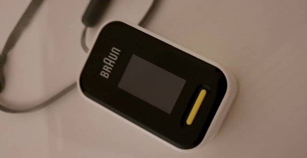 Nahaufnahme eines schwarz-weißen Braun Pulsoximeter im Test inklusive gelber Taste und schwarzem Kabel auf einer hellen Fläche.