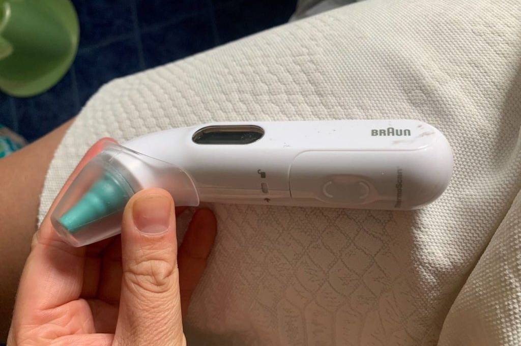 Getestetes Fieberthermometer in Weiß der Marke Braun inklusive LCD-Anzeige und Ohr-Endstück in Grün wird von einer Hand gehalten.