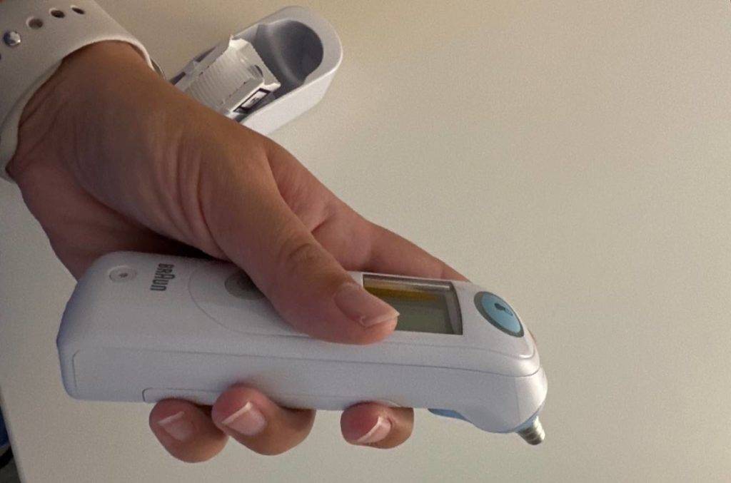Hand hält ein weißes, getestetes Fieberthermometer IRT6515 Thermoscan 6 von Braun vor weißer Fläche.