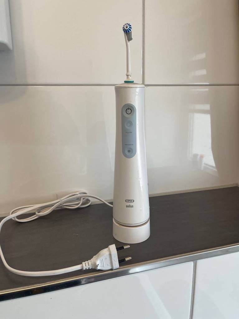 Getestete Munddusche der Marke Braun Oral-B im weiß-grauen Design steht inklusive Ladestation im Badebereich.