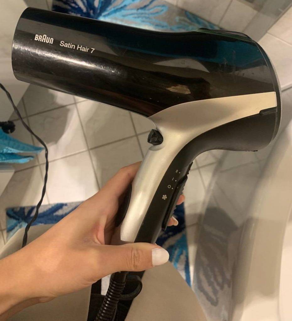 Hand hält einen Ionen-Haartrockner im Badezimmer.