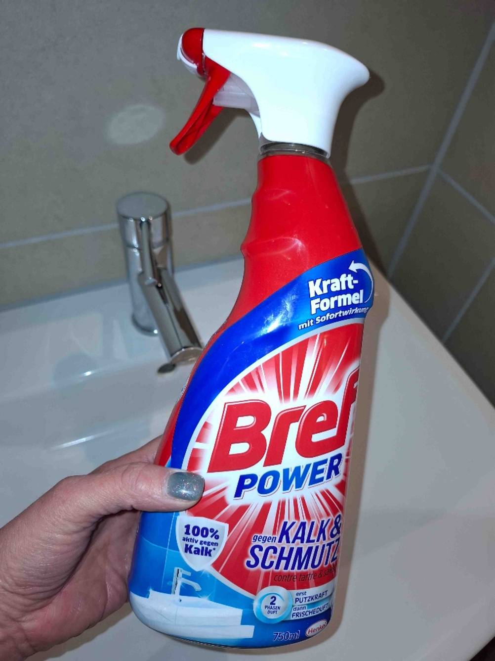 Eine Hand hält einen getesteten Badreiniger über einem Waschbecken.