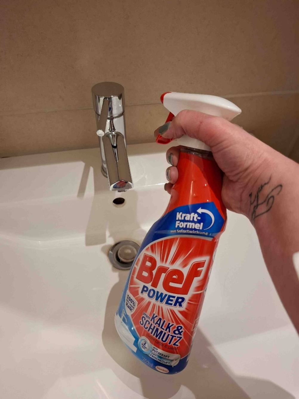 Eine Hand sprüht den getesteten Badreiniger im Pumpspender auf einen Wasserhahn.