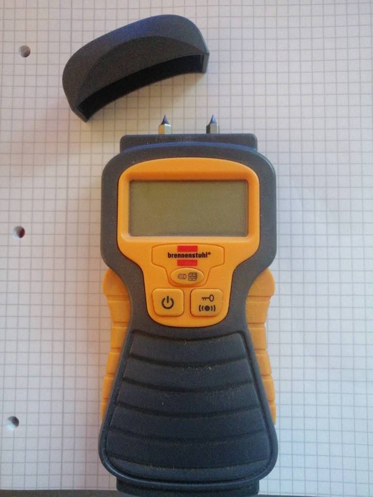 Ein schwarz-gelbes, getestetes Feuchtigkeitsmessgerät von Brennenstuhl liegt ausgeschaltet, neben seiner abgenommenen, schwarzen Schutzkappe, auf Rechenpapier.