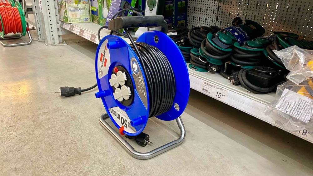 Eine Kabeltrommel 50m im Test von schräg seitlich vor einem Verkaufsregal mit anderen Produkten.