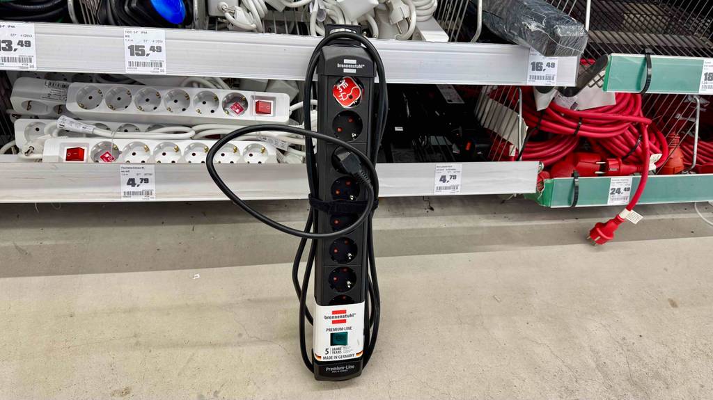 Eine getestete Steckdosenleiste (8-fach) in Schwarz steht vor einem Verkaufsregal mit Elektrozubehör.