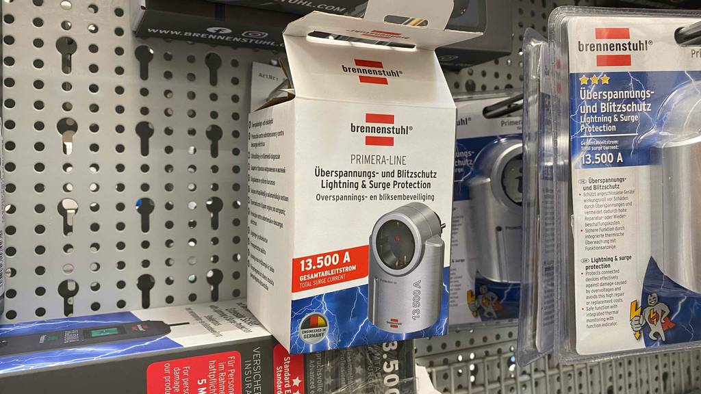 Eine Verpackung von einem metallfarbenem getesteten Überspannungsschutz und Blitzschutz von Brennenstuhl hängt neben weiteren Produkten an einem Verkaufsstand.