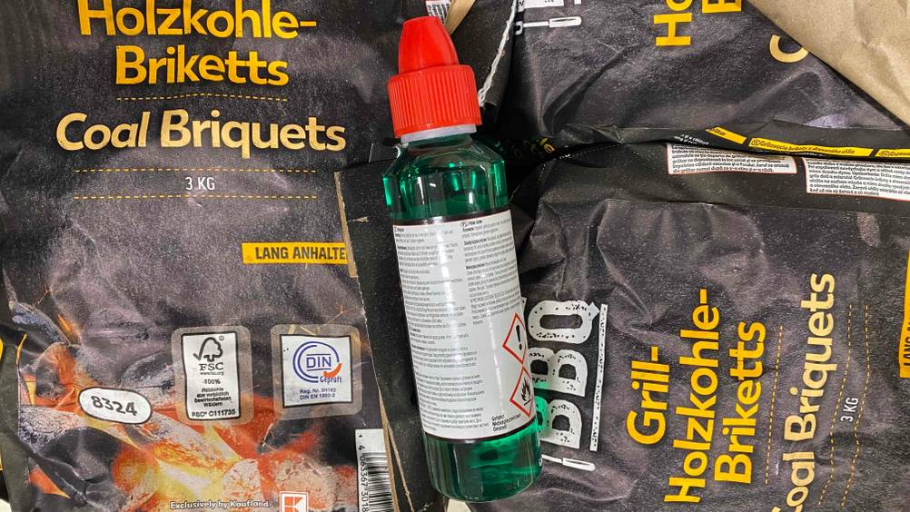 Im Test: Rückseite einer Flasche Brennpaste mit Warnhinweisen auf Packeten mit Holzkohle liegend.