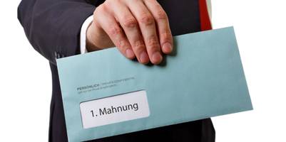 Eine Hand hält einen Briefumschlag mit dem Aufdruck Mahnung.