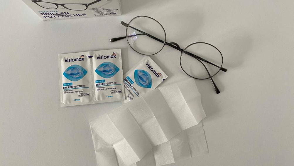 Auf einer hellen Oberfläche liegen eine Birille, drei Einzelverpackungen mit den getesteten Brillenputztüchern und ein Ausgepacktes.