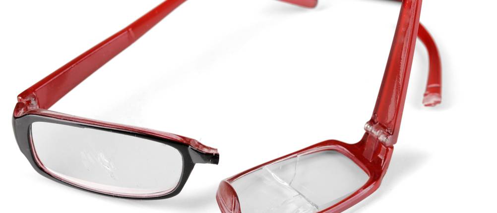 Vergleich der Brillenversicherungen: Eine zerbrochene rote Brille liegt auf einem weißen Untergrund.