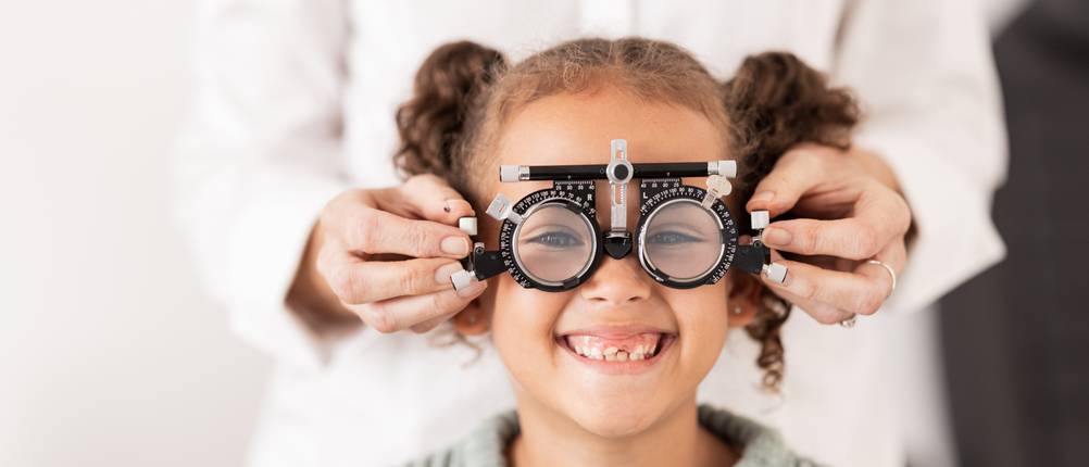 Ein Mädchen bekommt eine einstellbare Testbrille beim Optiker aufgesetzt.