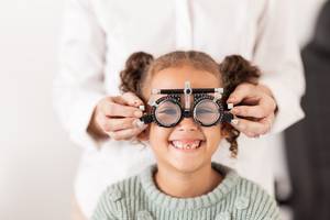Brillenversicherungen getestet: Ein Mädchen bekomt eine einstellbare Testbrille beim Optiker aufgesetzt.