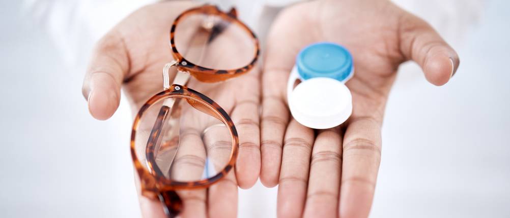 Brillenversicherungen im Test: Eine Brille und ein Kontaktlinsenbehälter liegen auf den Handflächen von zwei ausgestreckten Händen.