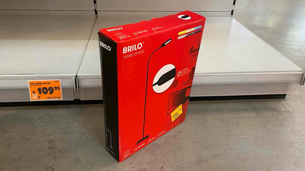 Getestet: Originalkarton einer Stehlampe fürs Büro steht schräg vor einem leeren Regal.