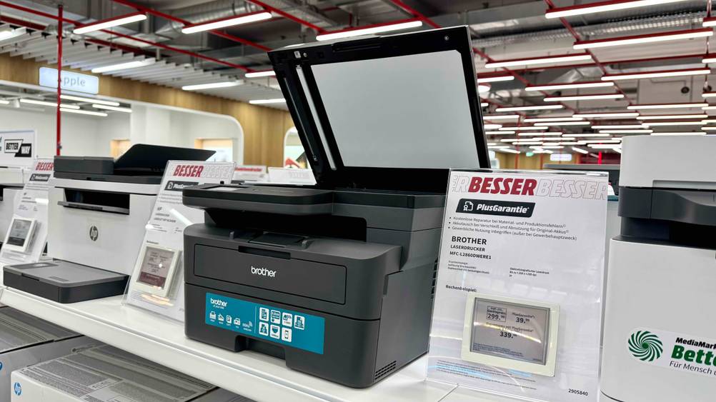 Brother-Laserdrucker-Test: Ein Gerät mit geöffneter Klappe auf einem Regal neben anderen Produkten stehend.