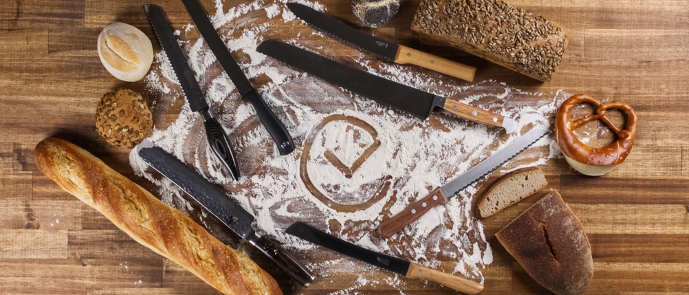 Brotmesser im Test: Brot und Messer liegen im Kreis auf einer Holzarbeitsplatte.
