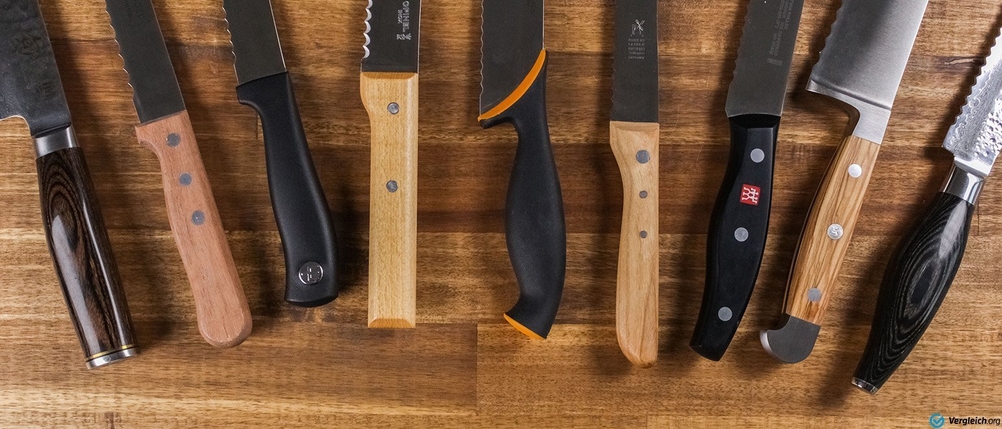 Brotmesser im Test: Brotmesser auf einer Holz-Arbeitsfläche. Im Fokus stehen die verschiedenen Griffe.