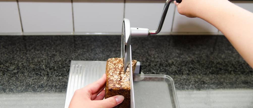 Brot wird mit einer getesteten, manuellen Brotschneidemaschine mit Kurbel geschnitten.