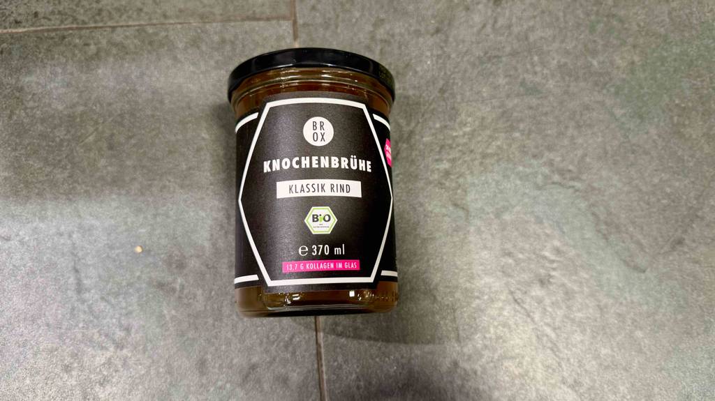 Getestete Knochenbrühe im Glas mit Schraubverschluss liegt auf einer grauen Oberfläche.