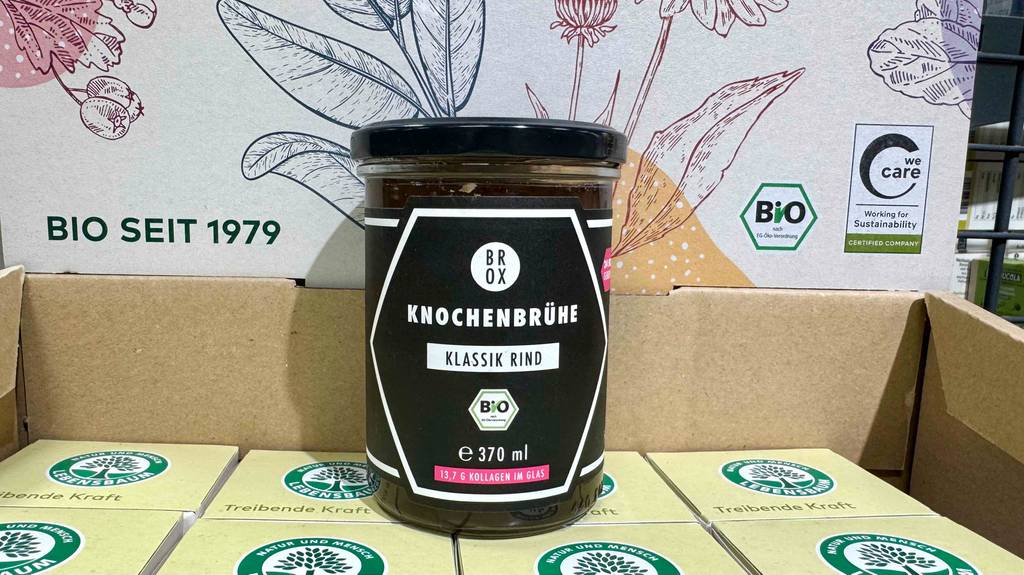 Getestete Knochenbrühe im 370-ml-Glas inklusive Schraubverschluss steht auf einem Lebensmittelkarton.