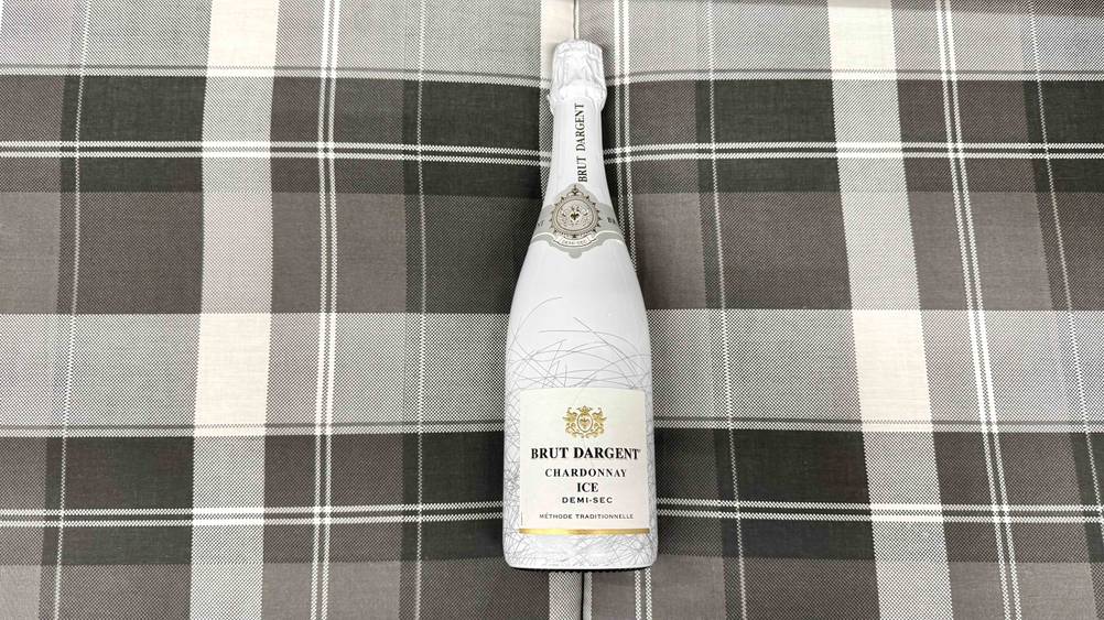 Eine Flasche des getesteten Brut-Dargent-Sekts auf einer karierten Fläche liegend.