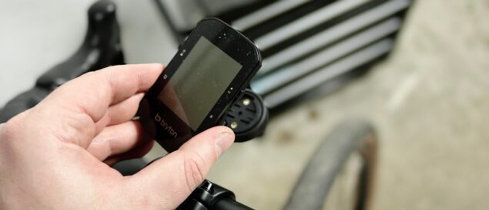 Ein Bryton Rider S500 wird per Hand in eine Fahrradhalterung eingesetzt. Das Rad steht in einer Garage mit Werkzeugschrank im Hintergrund.