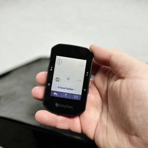 Das Display des Bryton Rider S500 zeigt eine Karte mit der Positionserfassung. Die Hand hält das Gerät über einer dunklen Tischoberfläche.