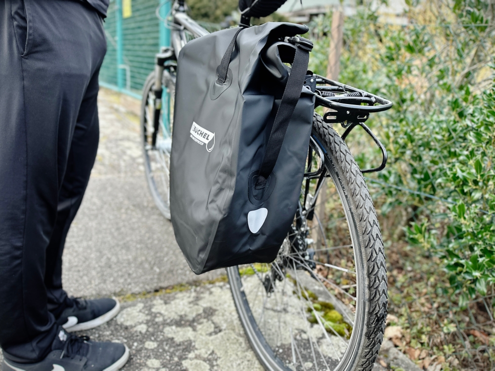 Seitlicher Blick auf die montierte Büchel-81518001-Tasche mit gut sichtbarem Reflektor an der Außenseite. Das Fahrrad steht auf einem Bürgersteig.
