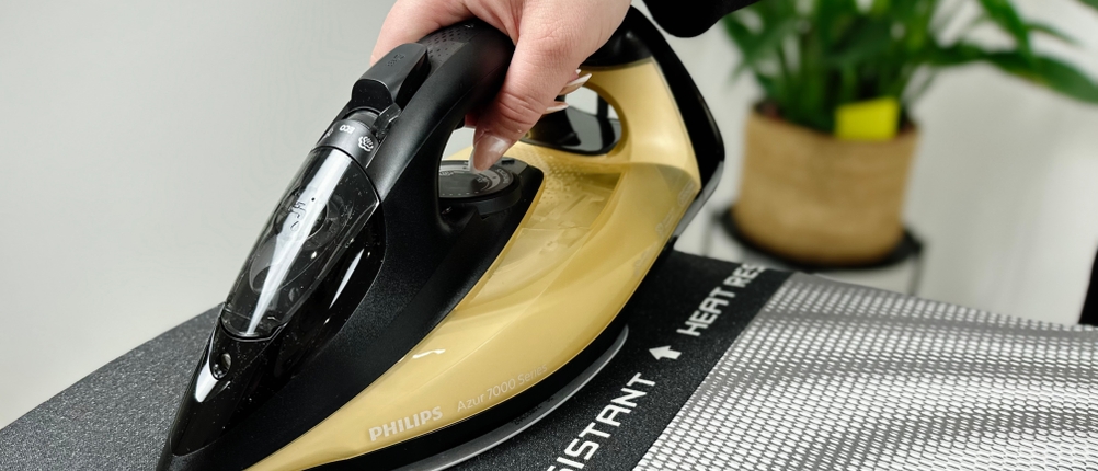 Eine Person stellt ein Bügeleisen auf die hitzebeständige Ablage auf dem Brabantia-345647J-Bügelbrett.