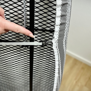 Eine Person zeigt auf die Befestigung des Bezugs am Brabantia-345647J-Bügelbrett. Der Bezug ist mit einem Clip gesichert.