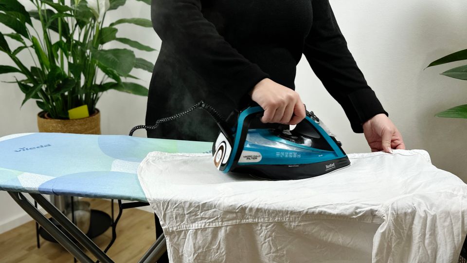 Eine Person bügelt ein weißes Kleidungsstück mit einem Tefal Dampfbügeleisen auf dem Vileda 161484 Bügelbrett. Dampfschwaden steigen auf.