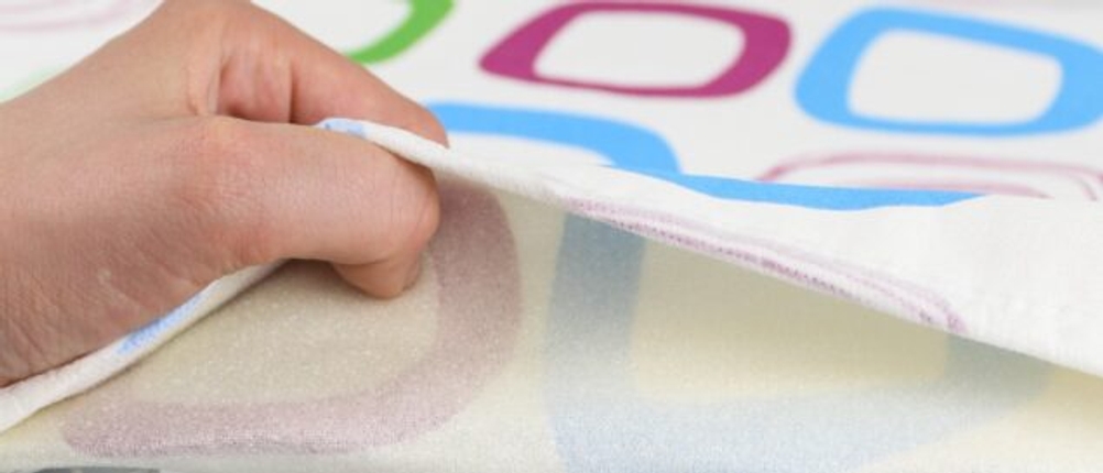 Eine Hand greift einen Bügelbrettbezug und zieht ihn vom Bügelbrett